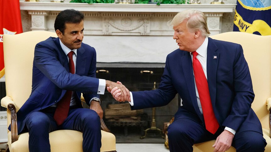 President Donald Trump shakes hands with Qatar's Emir as they sit on two yellow chairs at the White House.