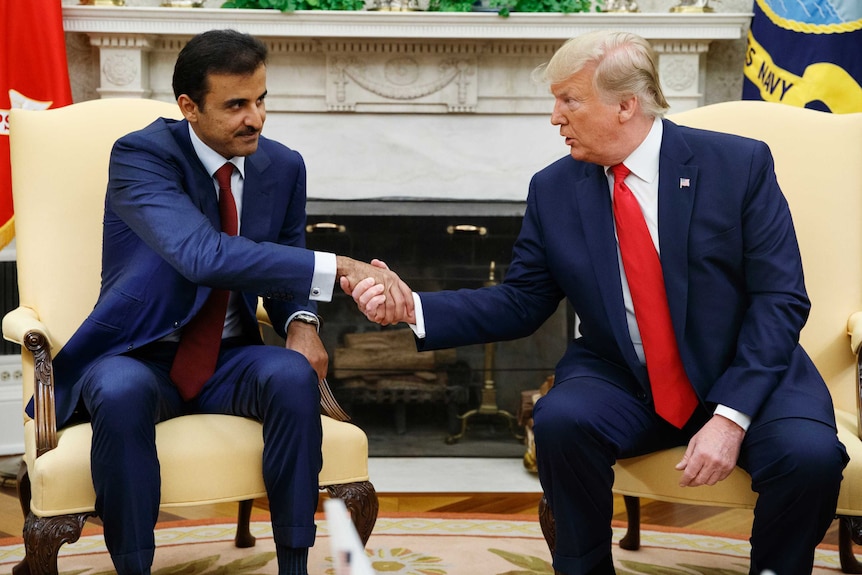 President Donald Trump shakes hands with Qatar's Emir as they sit on two yellow chairs at the White House.