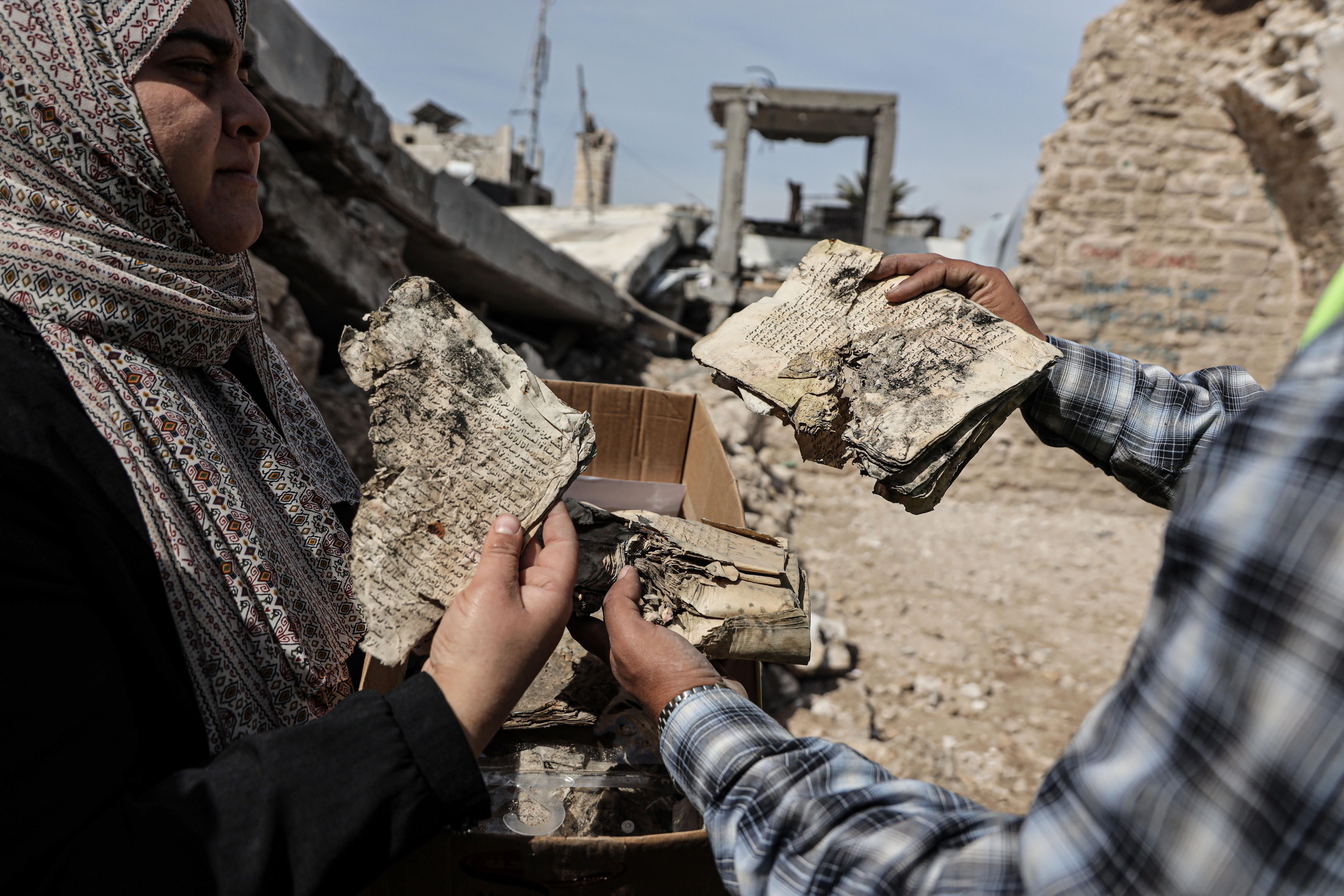 A woman wearing a hijab examines the brittle pages of a book while another man holds the book.