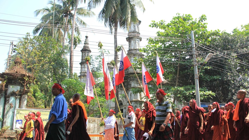 Monks and other protesters holding flags walk past a mosque.