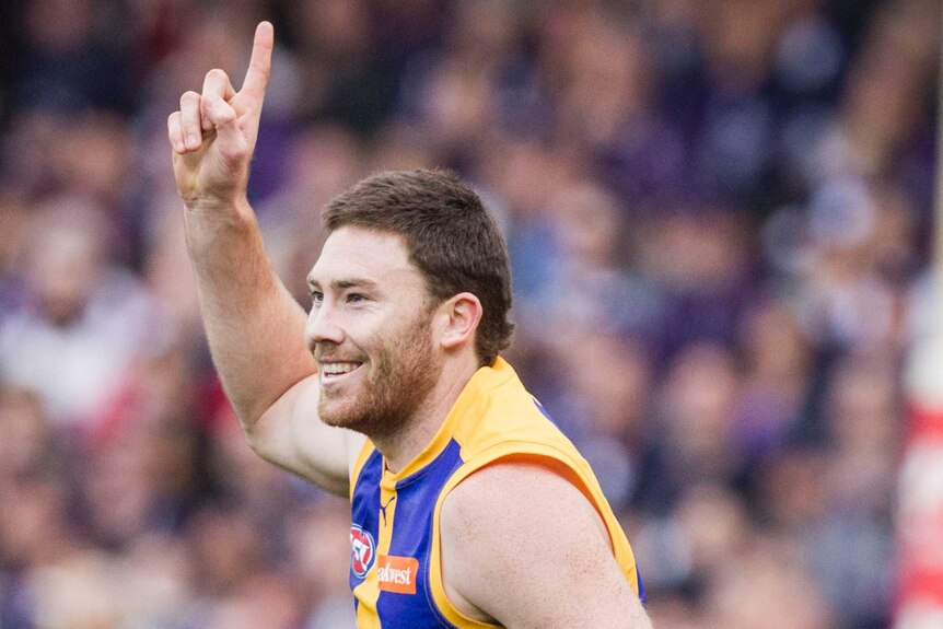 A happy Eagles defender Jeremy McGovern celebrates a goal with a finger in the air wearing West Coast's alternate yellow jumper.
