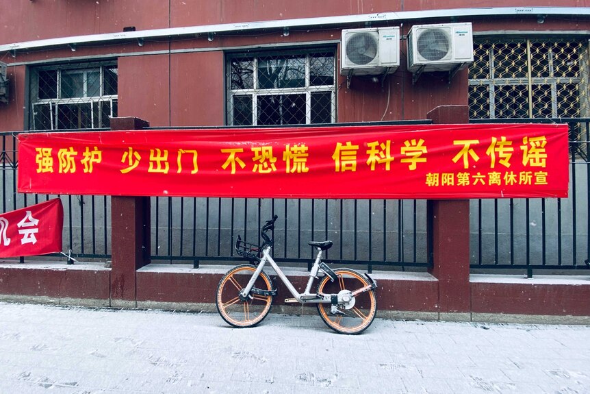 A red government banner with yellow Chinese characters hangs on a black fence.