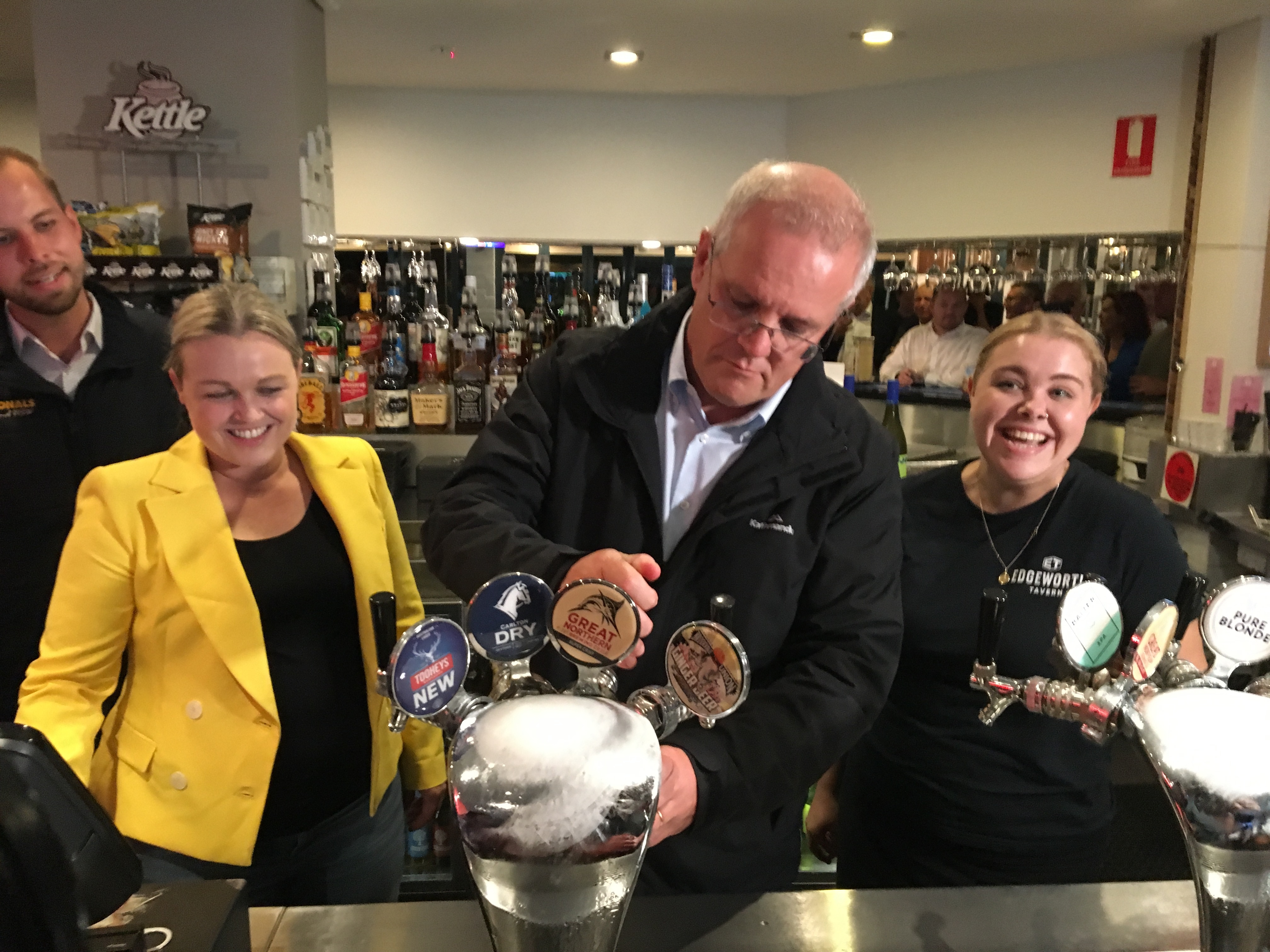 A man pours a beer from a tap in a pub with two smiling women either side.