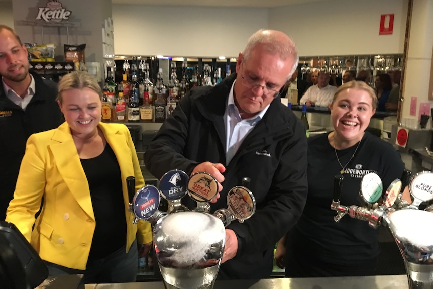 A man pours a beer from a tap in a pub with two smiling women either side.