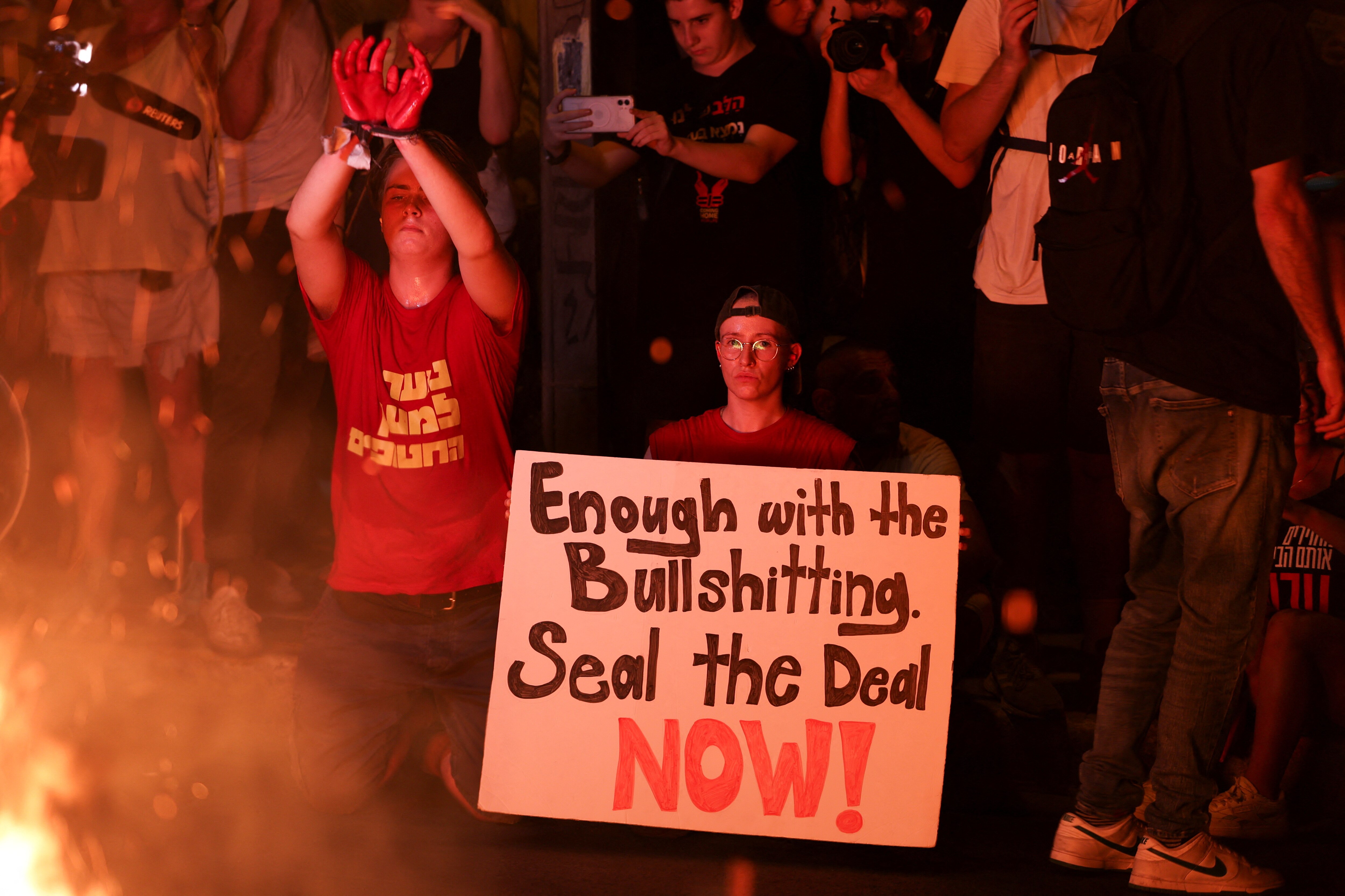 A person holding a sign reading "Enough with the bullshitting. Seal the deal now!" with a person in fake handcuffs next to them