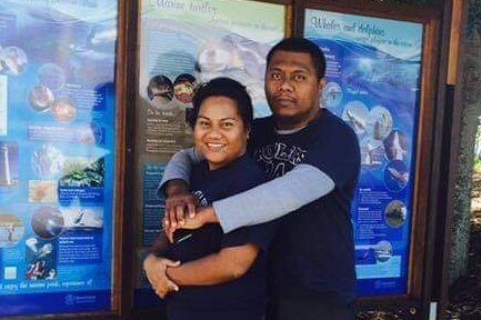 A woman and her husband embrace in front of a sign, in Hervey Bay. 