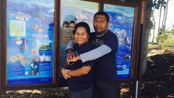 A woman and her husband embrace in front of a sign, in Hervey Bay. 