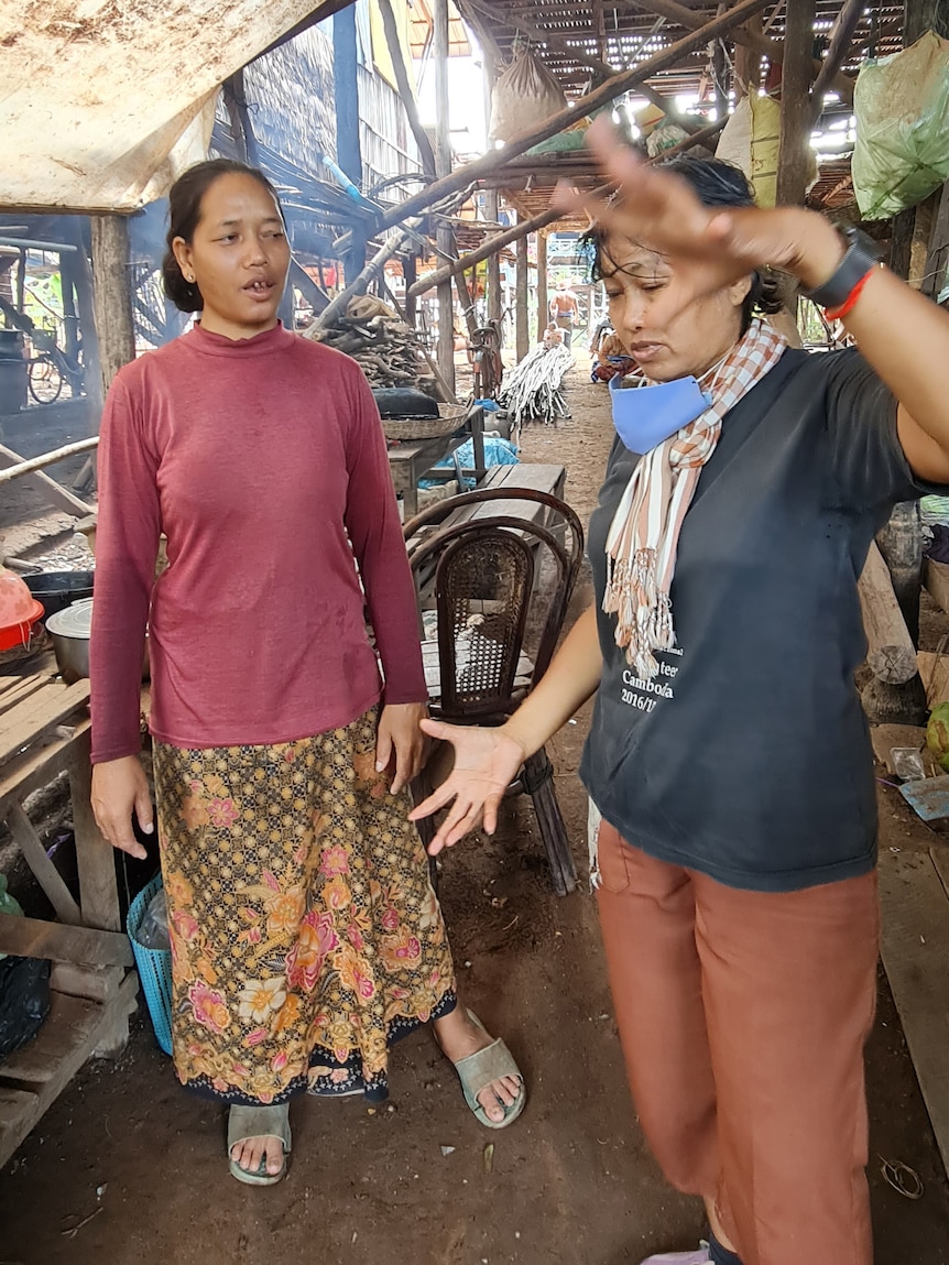 Tow Cambodian women talk outside, one wearing a long sleeve maroon top, the other a blue t-shirt.