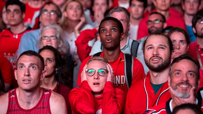 A group of people dressed in red team colours watch ahead with looks of intense anticipation and focus.