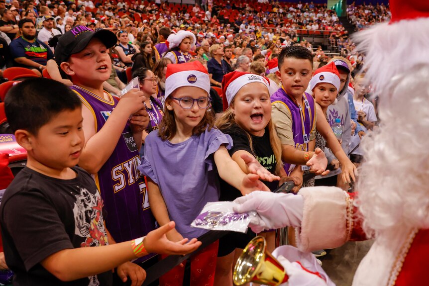 Children wearing purple shirts and Santa hats receive gifts during a basketball game