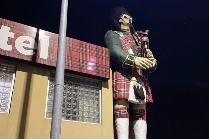 A large statue of a Scotsman playing the bagpipes with googly eyes