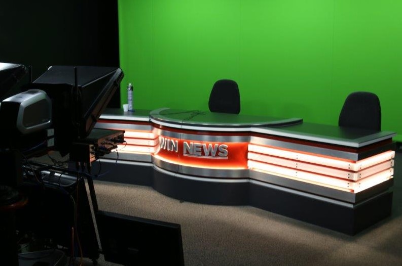 An unmanned WIN News studio, with green lighting in the background.