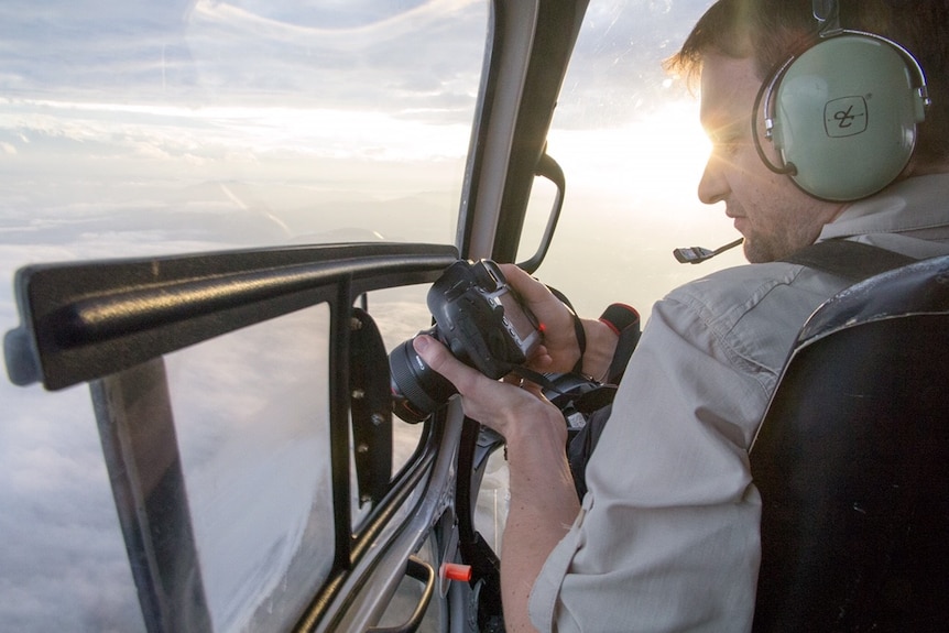 Luke Gibbs taking aerial photographs from inside helicopter at sunset.