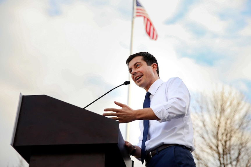 Mayor Pete Buttigieg talking at a podium with the American flag behind him