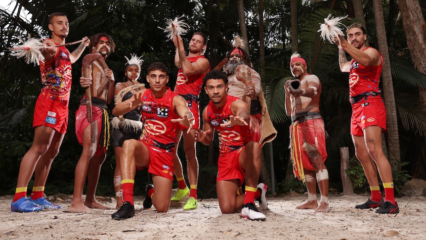 Gold Coast players wearing the club's Indigenous round jersey with men in ceremonial clothing and body paint. 