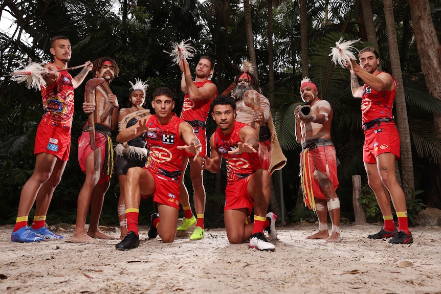 Gold Coast players wearing the club's Indigenous round jersey with men in ceremonial clothing and body paint. 