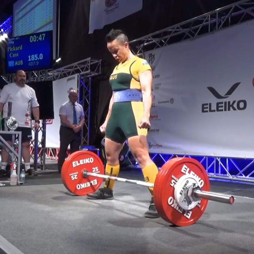 A woman powerlifter stands with weights in front of her, she is wearing Australian representative clothing.