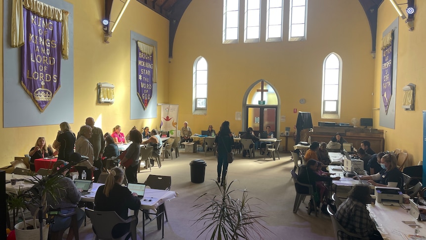 Chuch hall interior with light coming through windows and tables with people at them set up inside.