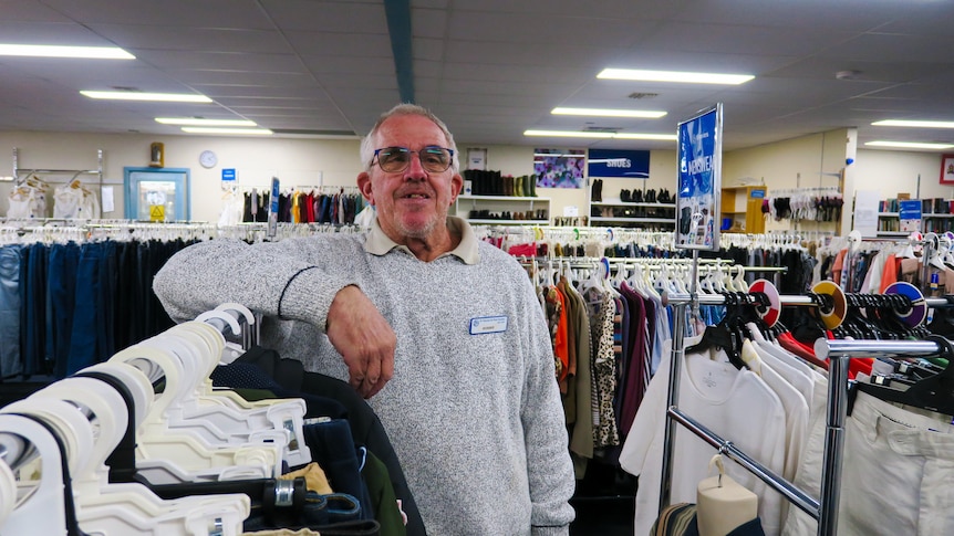 An older man in a hoodie stands smiling an op shop.