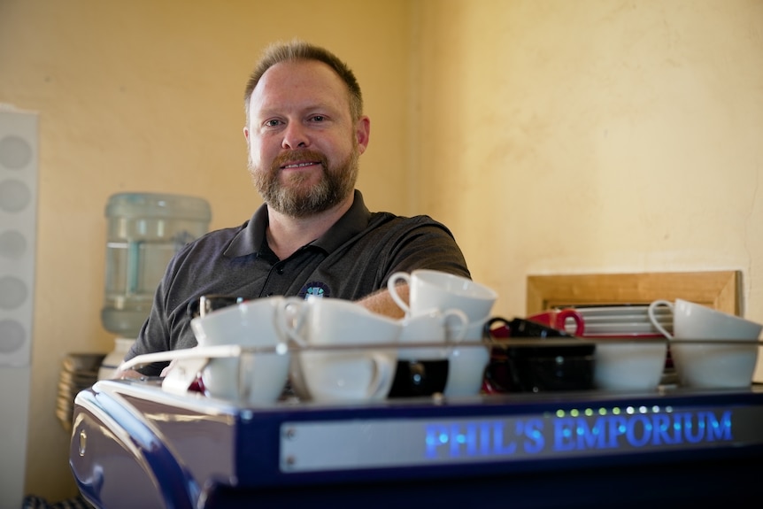 A man smiles behind a coffee machine.