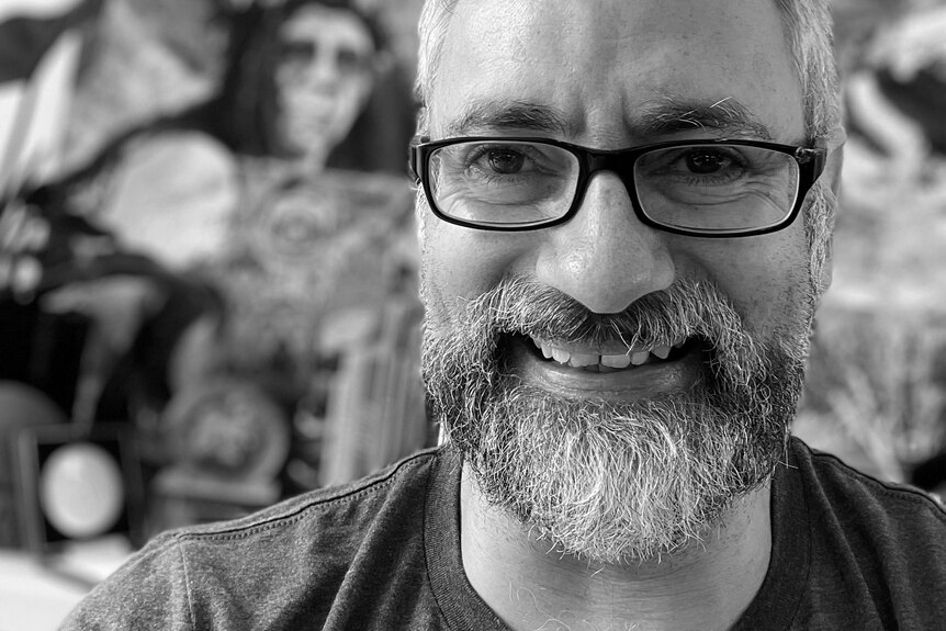 Una fotografía en blanco y negro de Dub Leffler con gafas de lectura, barba y bigote, sonriendo.