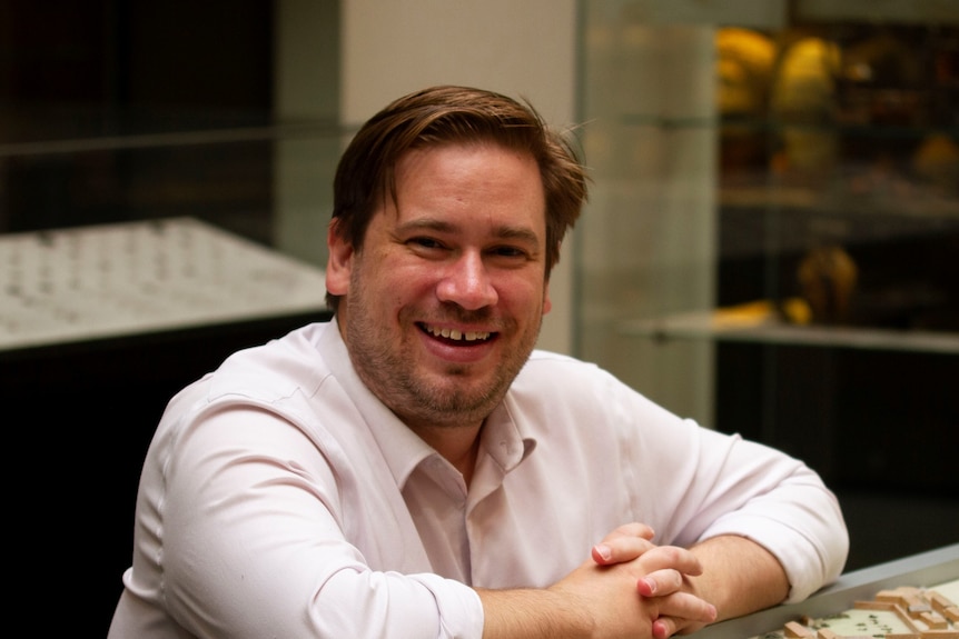 A man smiles wearing a white collared shirt.