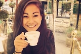 Mia Ayliffe Chung sitting at a table smiling while holding a cup of tea