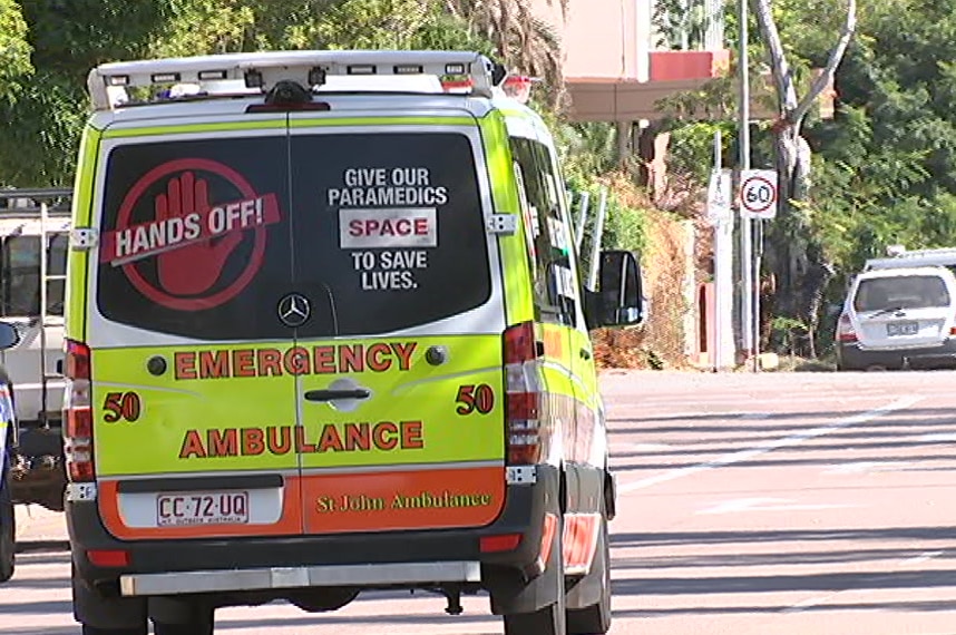 An NT ambulance driving down the street with a 'Hands Off' sign printed on the back.