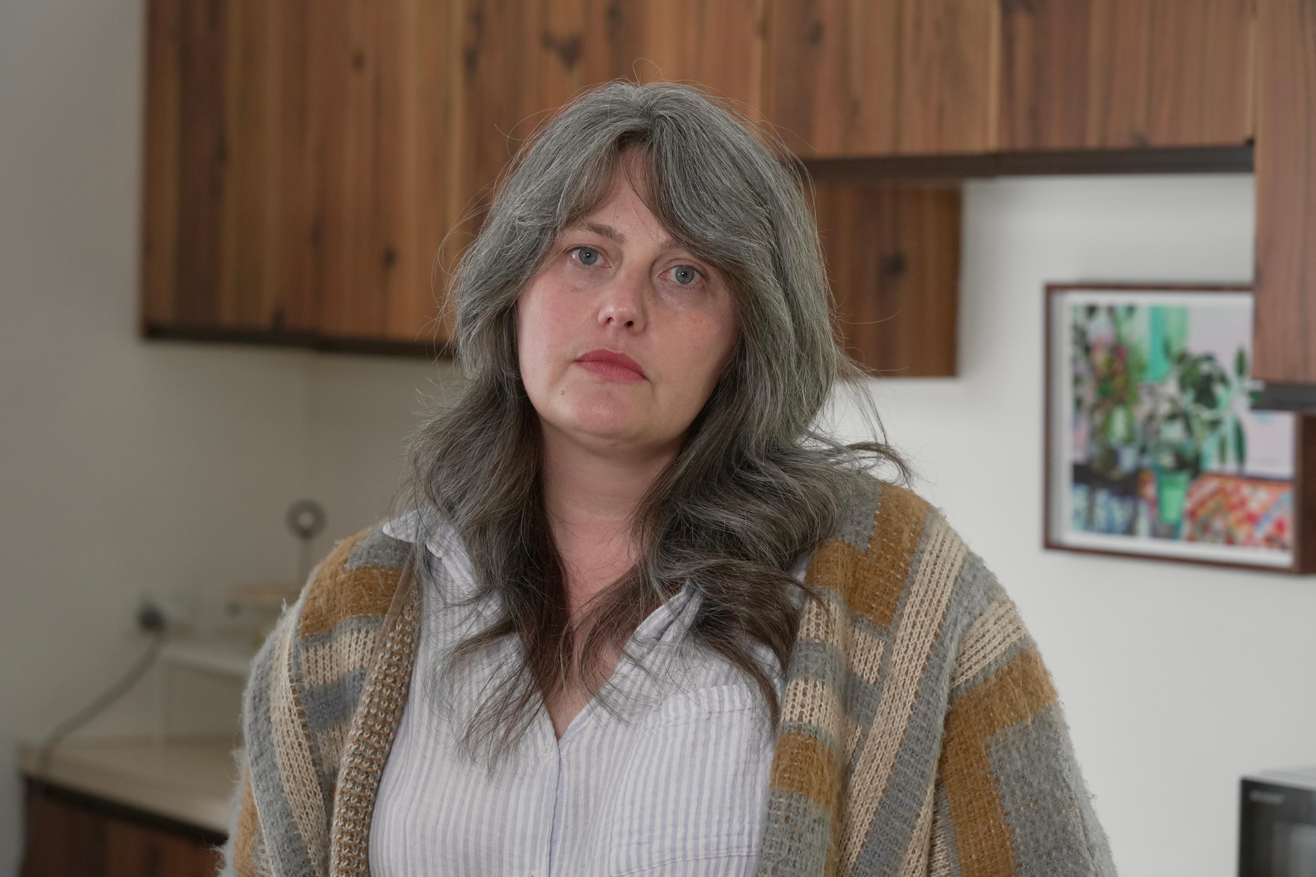 A white woman with greying brown hair standing in a kitchen with wooden cabinets