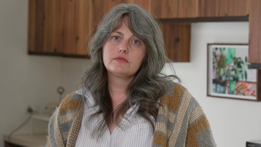 A white woman with greying brown hair standing in a kitchen with wooden cabinets