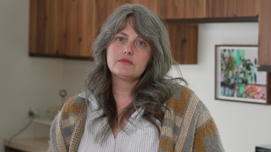 A white woman with greying brown hair standing in a kitchen with wooden cabinets