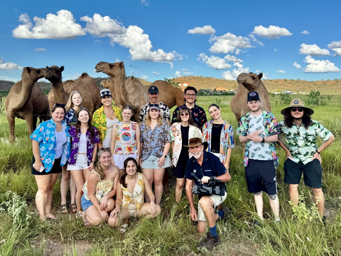 Jóvenes estudiantes sonrientes con camisas hawaianas se encuentran en un campo con cuatro camellos 