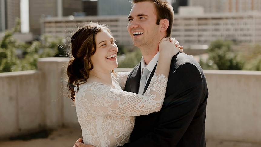 Couple in wedding outfits smile in an embrace