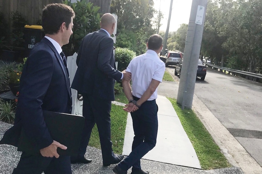 Two men lead a man in handcuffs to a car.