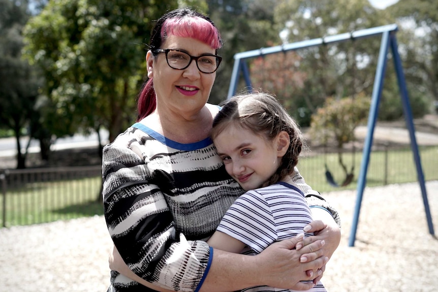 A woman hugging a girl in front of playground swings