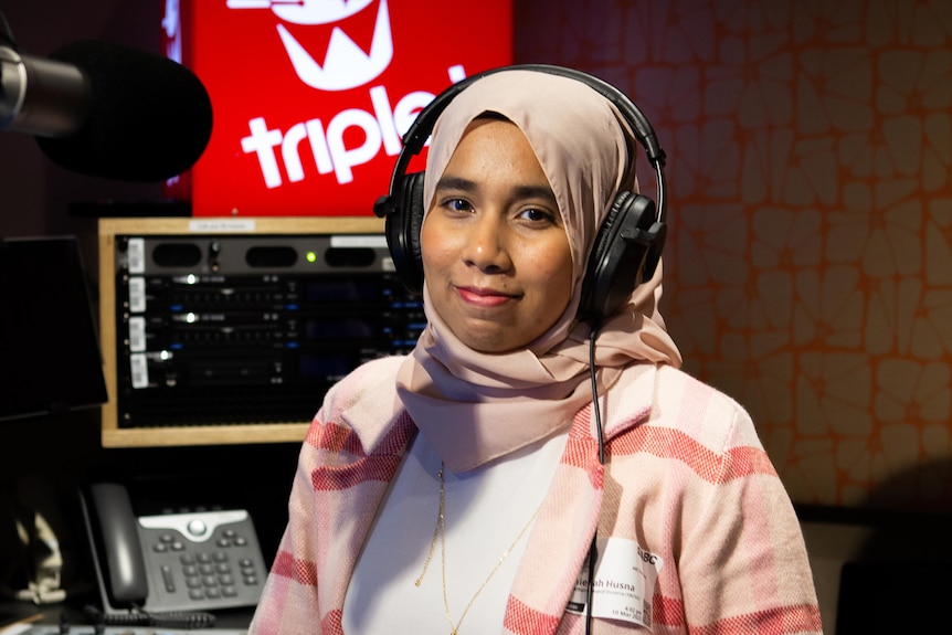 Girl wears pink headscarf and top and looks to the camera smiling. A red box with triple j and a drum in white is lit up.