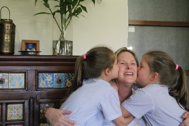 A smiling woman is kissed by two girls in school uniforms.