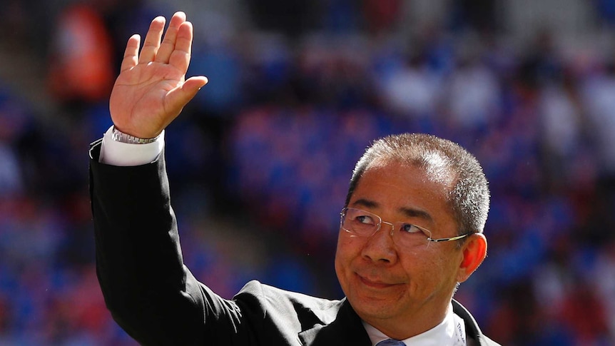 Vichai Srivaddhanaprabha with a neutral expression, waves, with a crowd blurred out in the background