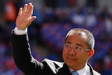 Vichai Srivaddhanaprabha with a neutral expression, waves, with a crowd blurred out in the background