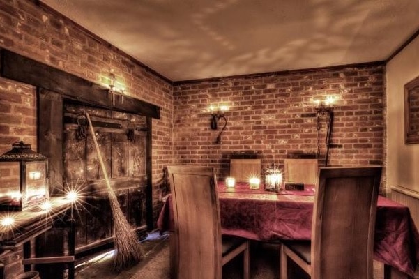 An interior shows brick walls, broom leaning against wall, and bright candles.