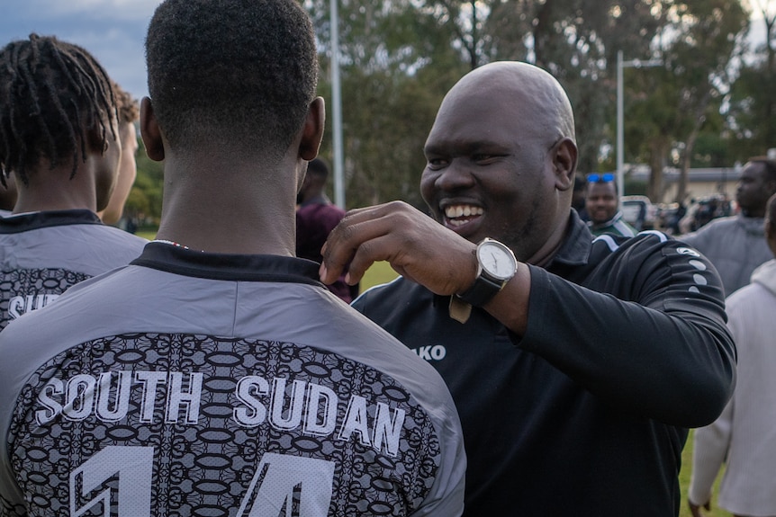 An African man smiling as he is about to embrace a soccer player