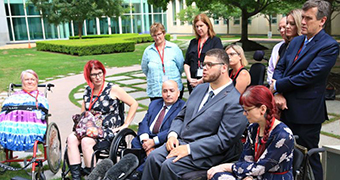 Five people in wheelchairs are gathered around a microphone.