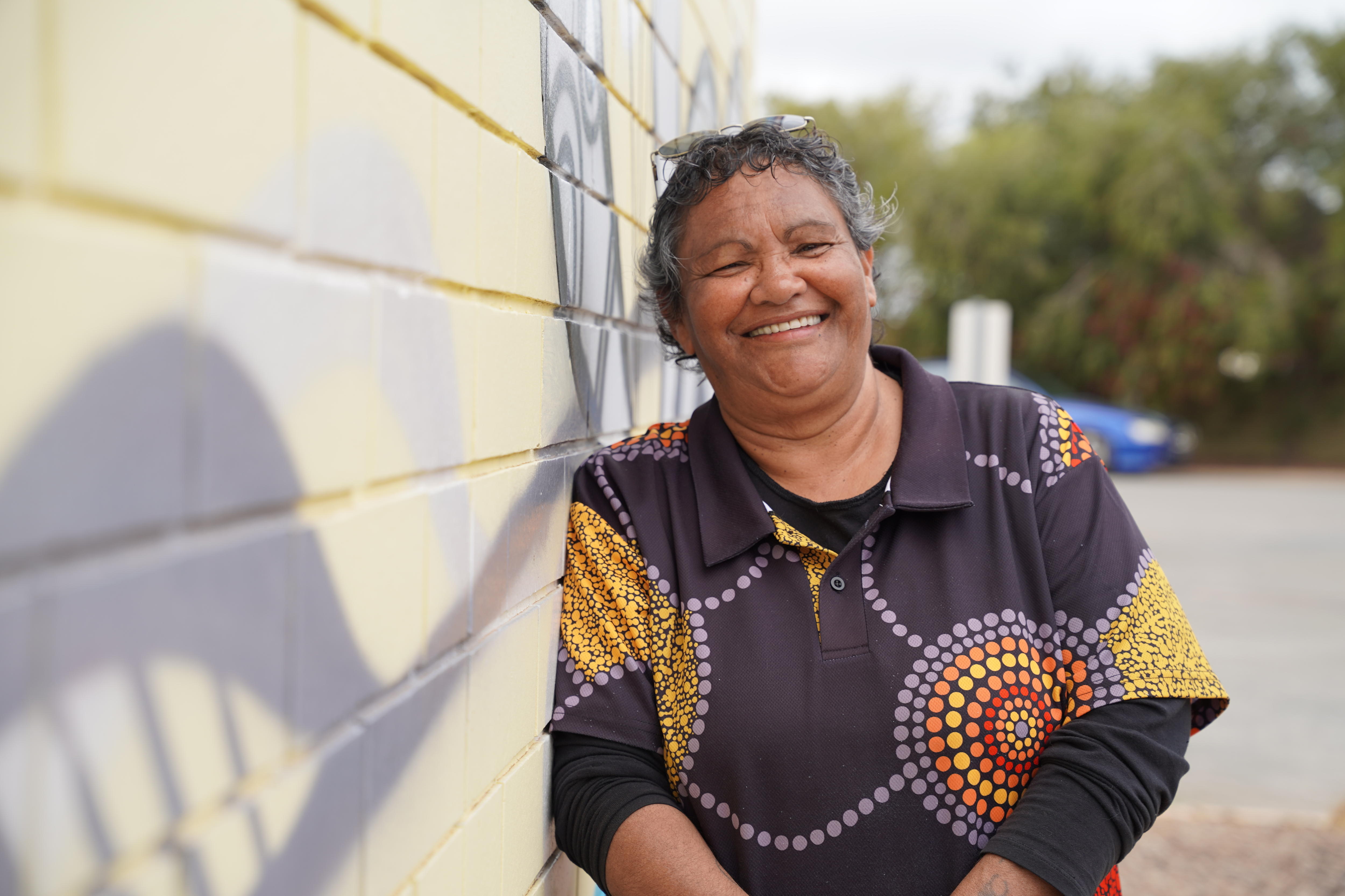 Una mujer aborigen se apoya contra una pared cubierta de obras de arte indígenas.