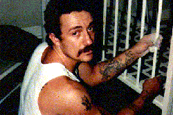 A man with tattoos in his arm, a white vest and a moustache