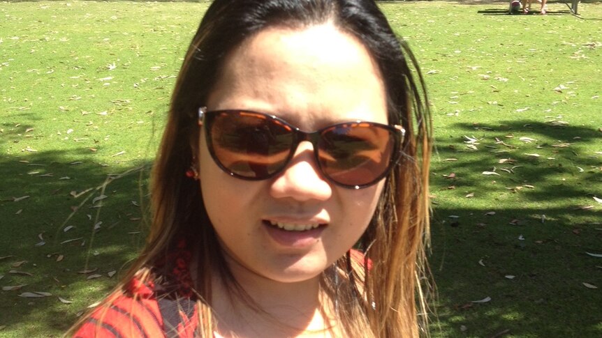 A woman wearing sunglasses at a park on a sunny day looks at the camera.