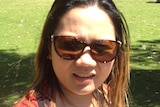 A woman wearing sunglasses at a park on a sunny day looks at the camera.