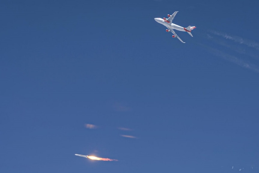 Flames shoot from a rocket which has just been dropped from beneath the wing of a jumbo jet.