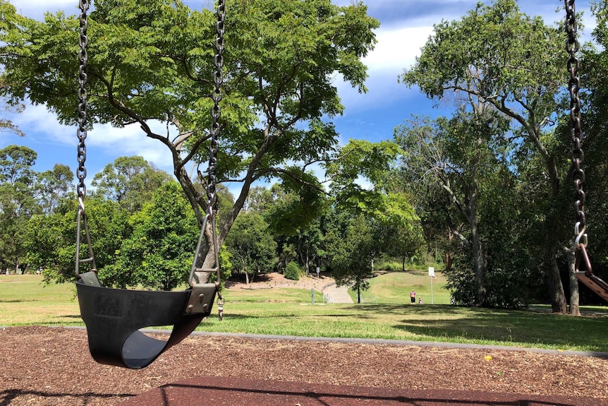 A children's swing in a park surrounded by trees.