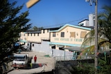 A cream and blue building stands behind a cement wall behind barbed wire in a Haitian street.