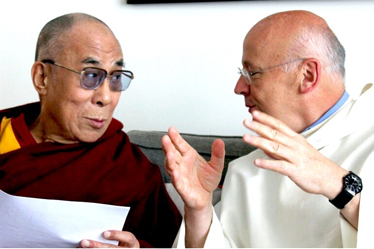 The Dalaim Lama in burgundy robes speaking to a friar in white robes